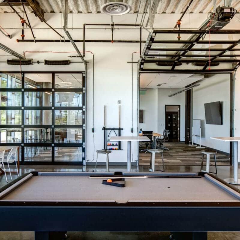 contemporary industrial office interior with tables, chairs, and a neutral pool table designed by Think Architecture