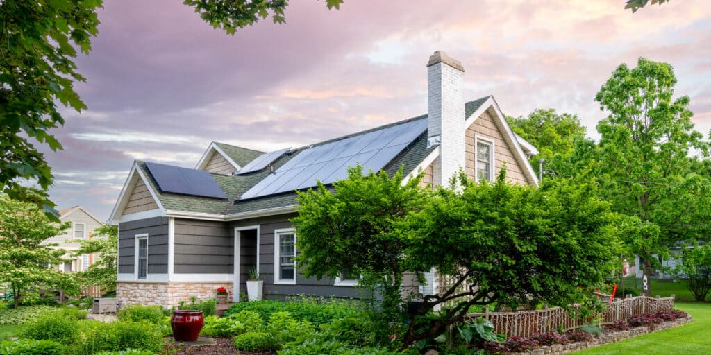 gray home surrounded by greenery & trees with solar panels on roof for energy efficient design
