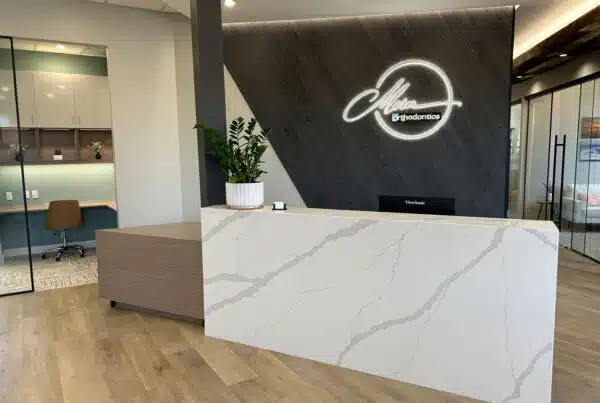 Front desk with quartz waterfall counter and illuminated logo wall, Meru Orthodontics reception, healthcare tenant improvement interior design by Think Architecture