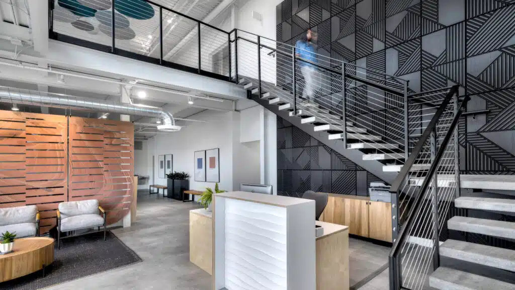 Tenant improvement project with open office reception, mezzanine staircase, and modern industrial finishes.